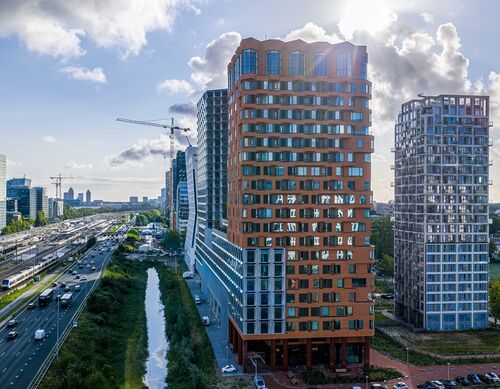 Utvendig visning av prosjektet The Pulse i Amsterdam med moderne høyhus og urban transportinfrastruktur.