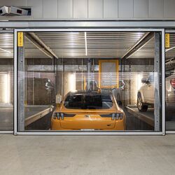 Bildet viser en gul sportsbil i et parkeringssystem inne i en moderne parkeringskjeller.